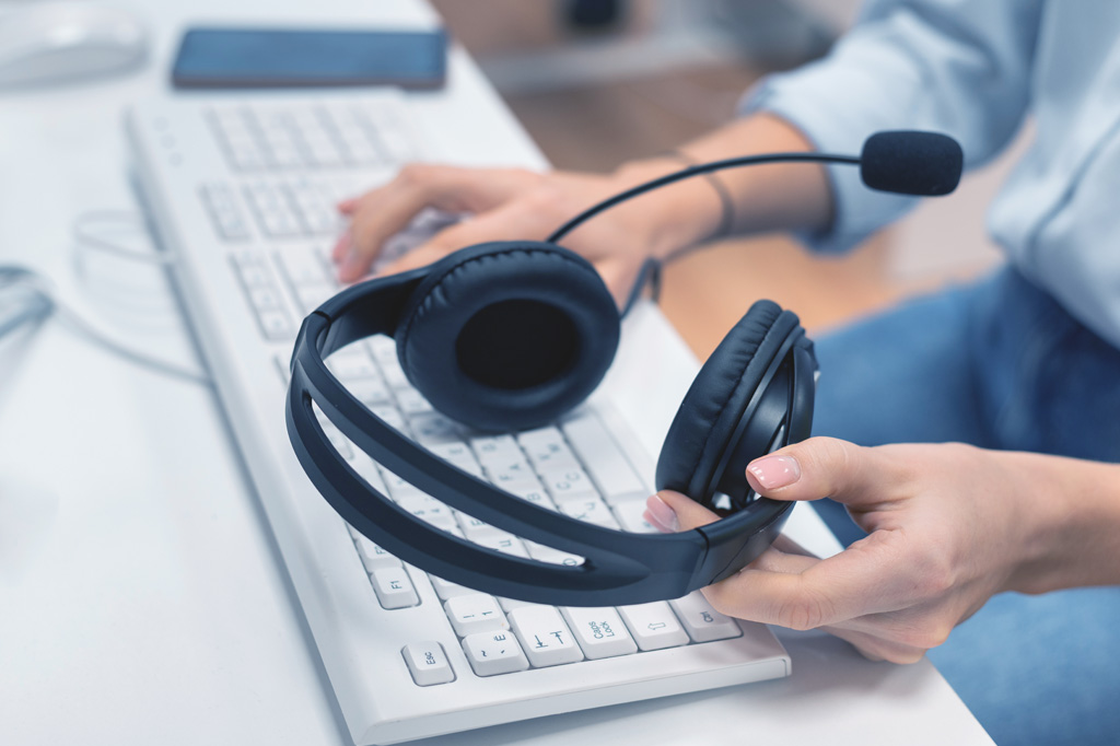 Zwei Hände die ein Headset halten und auf der Tastatur tippen